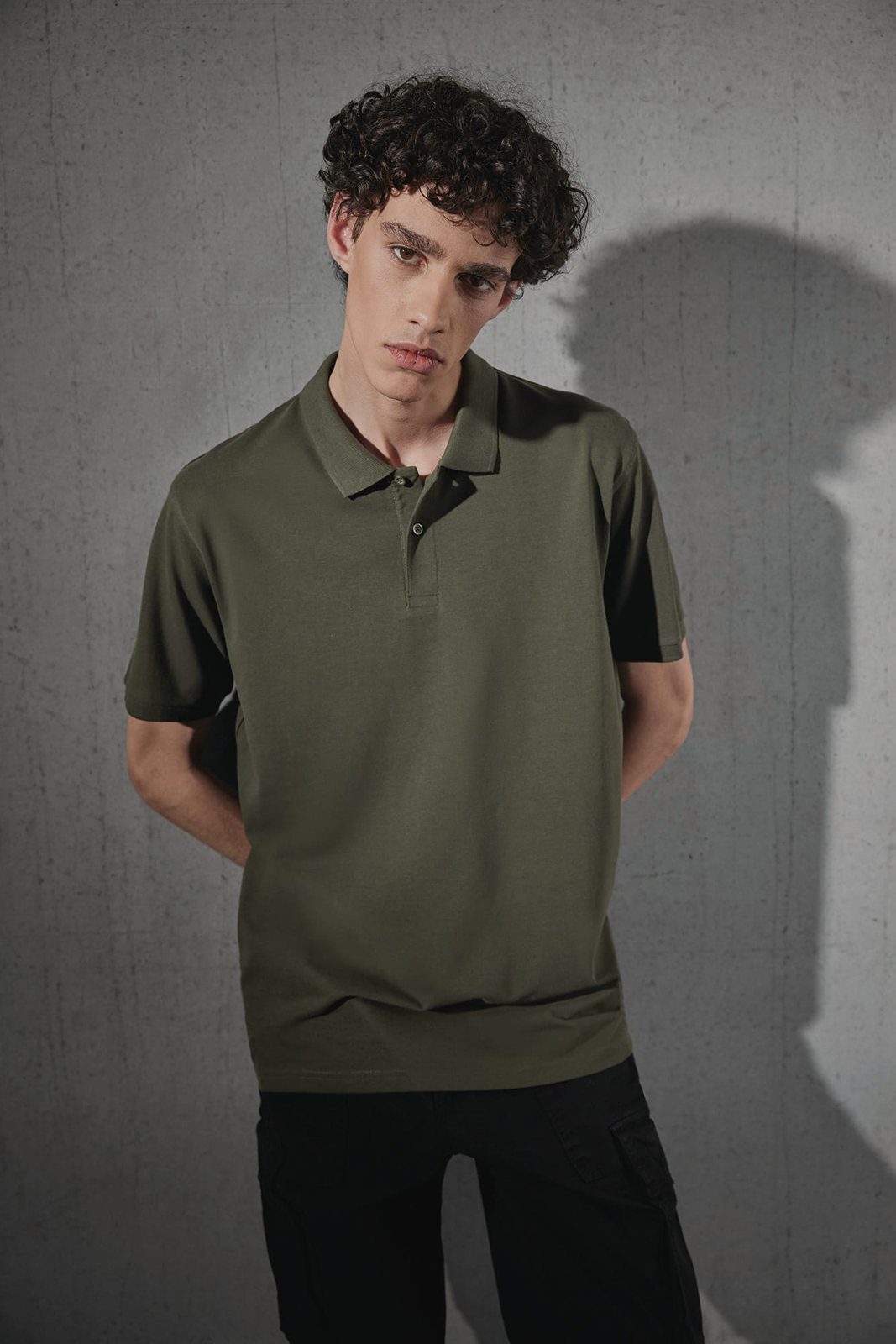 Jongeman met krullen in een olijfgroene polo, handen op de rug