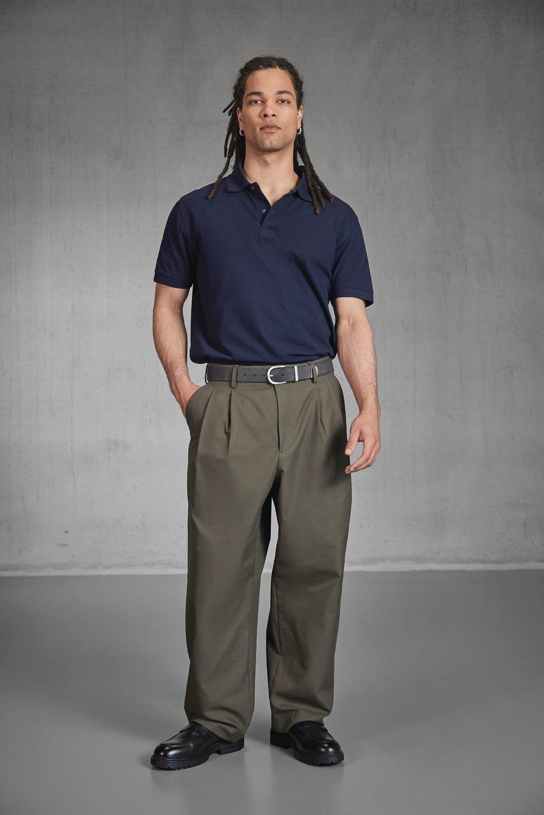 Man met lange vlechten in een donkerblauwe polo en een olijfgroene pantalon
