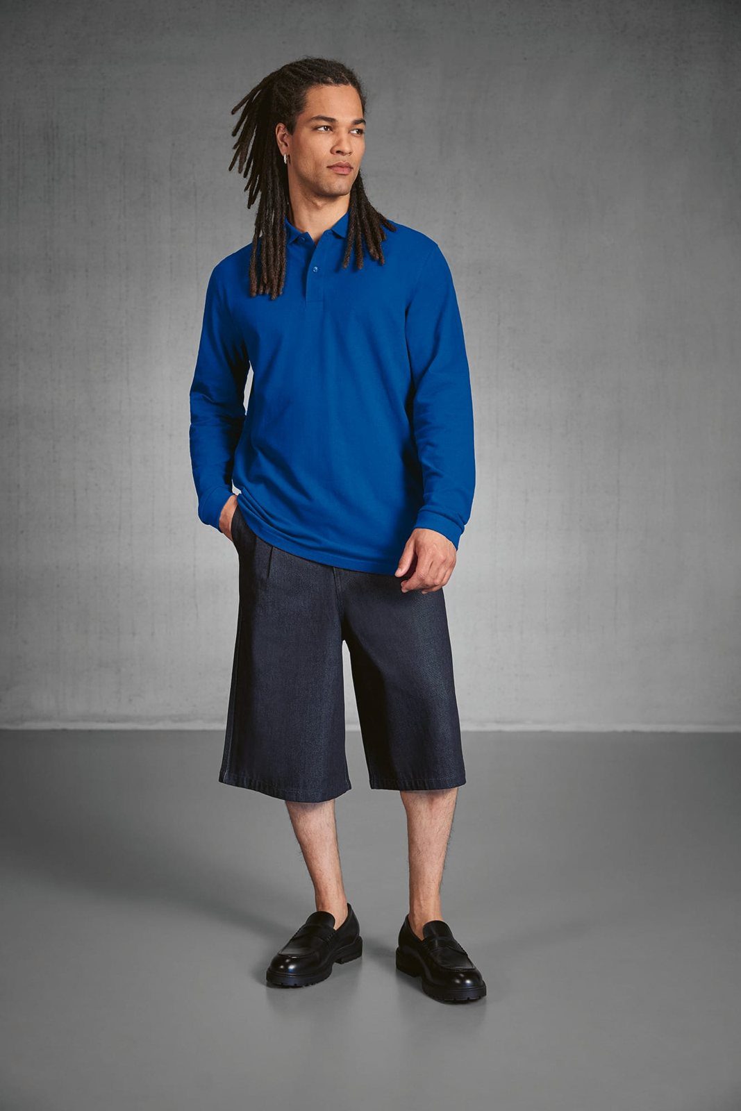 Man met dreadlocks in een koningsblauwe polo met lange mouwen en een korte broek