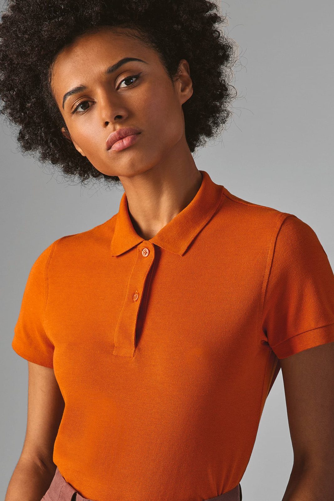 Vrouw met krullend haar in een oranje polo, close-up van kraag en knoopsluiting