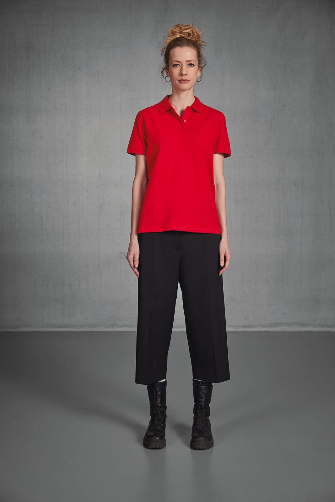 Vrouw met opgestoken haar in een rode polo en een zwarte cropped pantalon