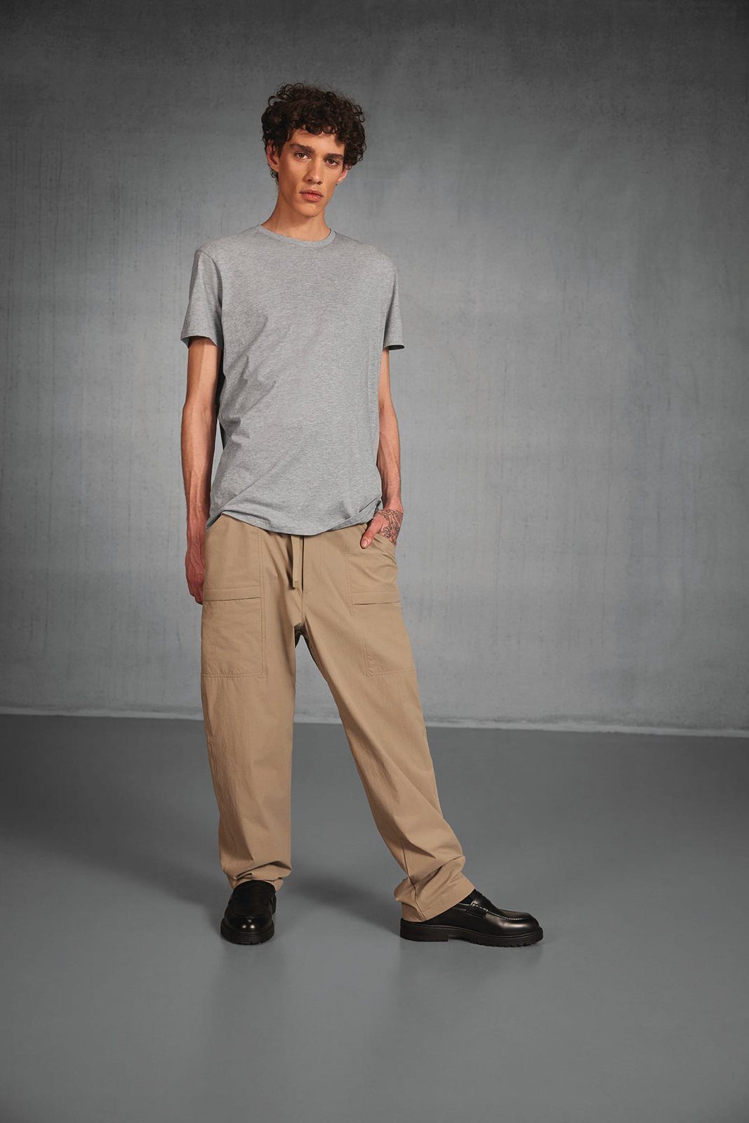 Jongeman in een lichtgrijs T-shirt, beige broek en zwarte schoenen