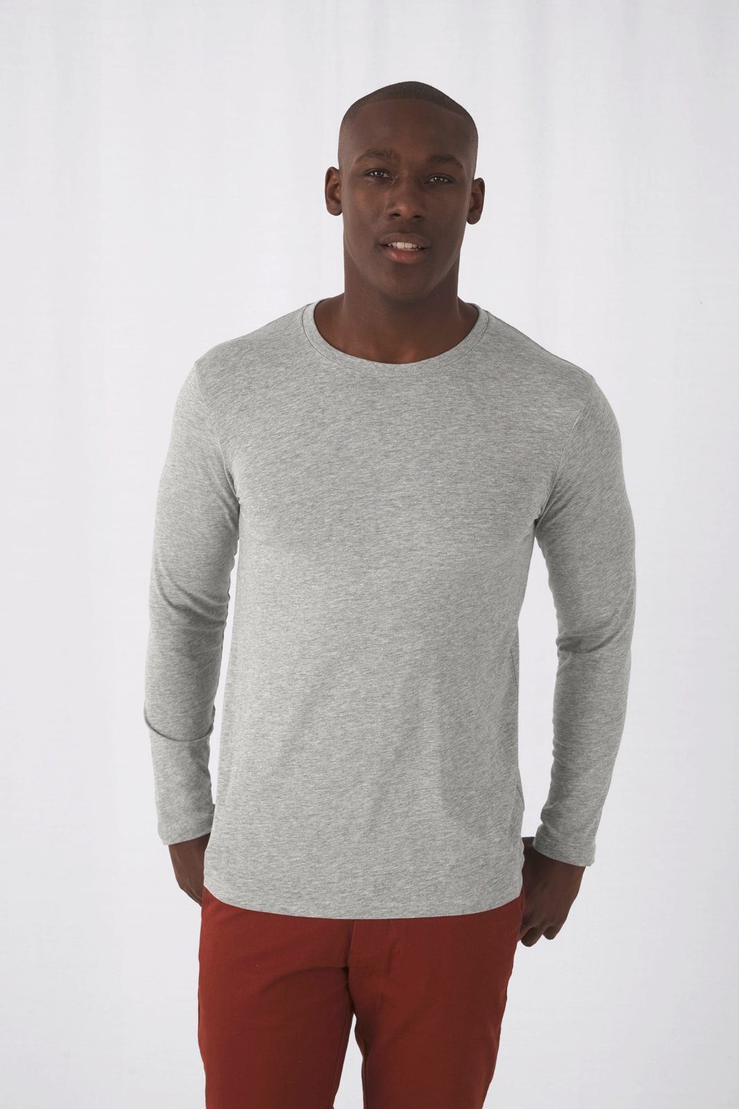 Man in een lichtgrijs gemêleerd shirt met lange mouwen en een roestrode broek