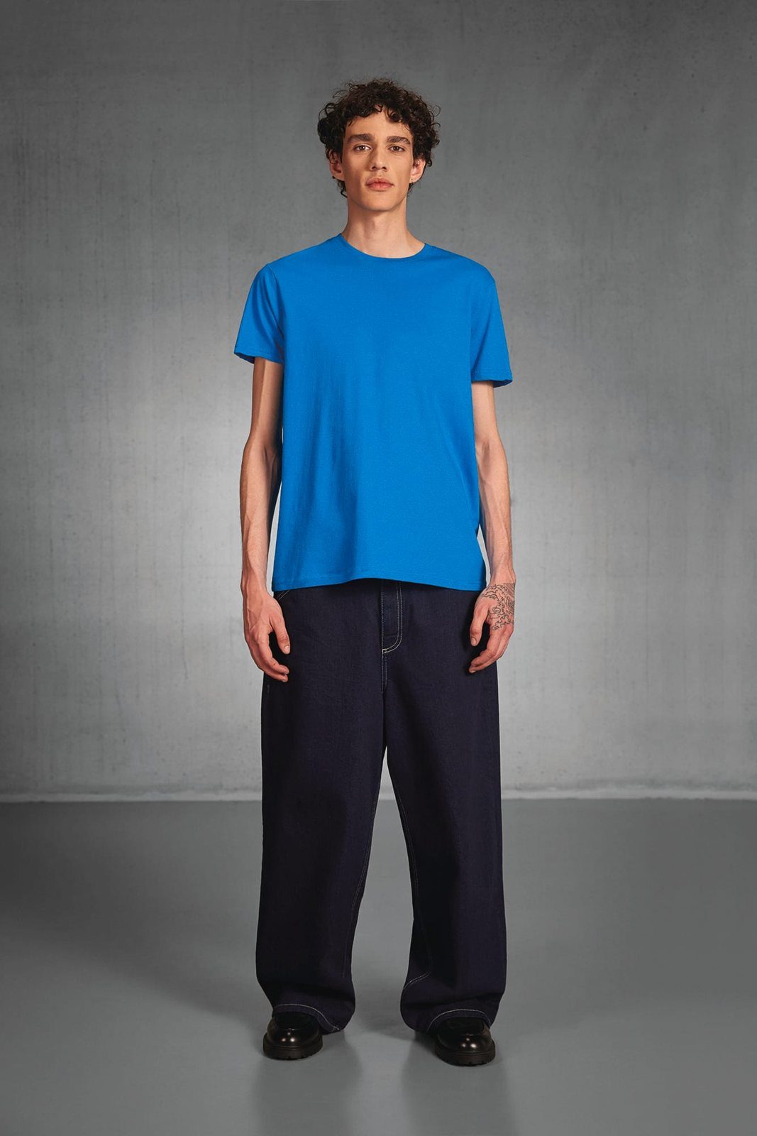 Jongeman in een felblauw T-shirt en een wijde donkere jeans in een grijze studio