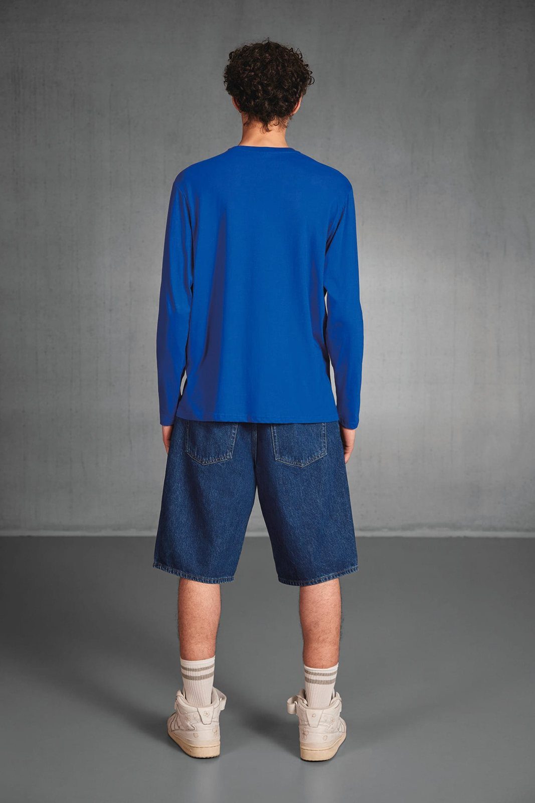 Achterkant van een man in een blauw shirt met lange mouwen, jeansshort en witte sokken
