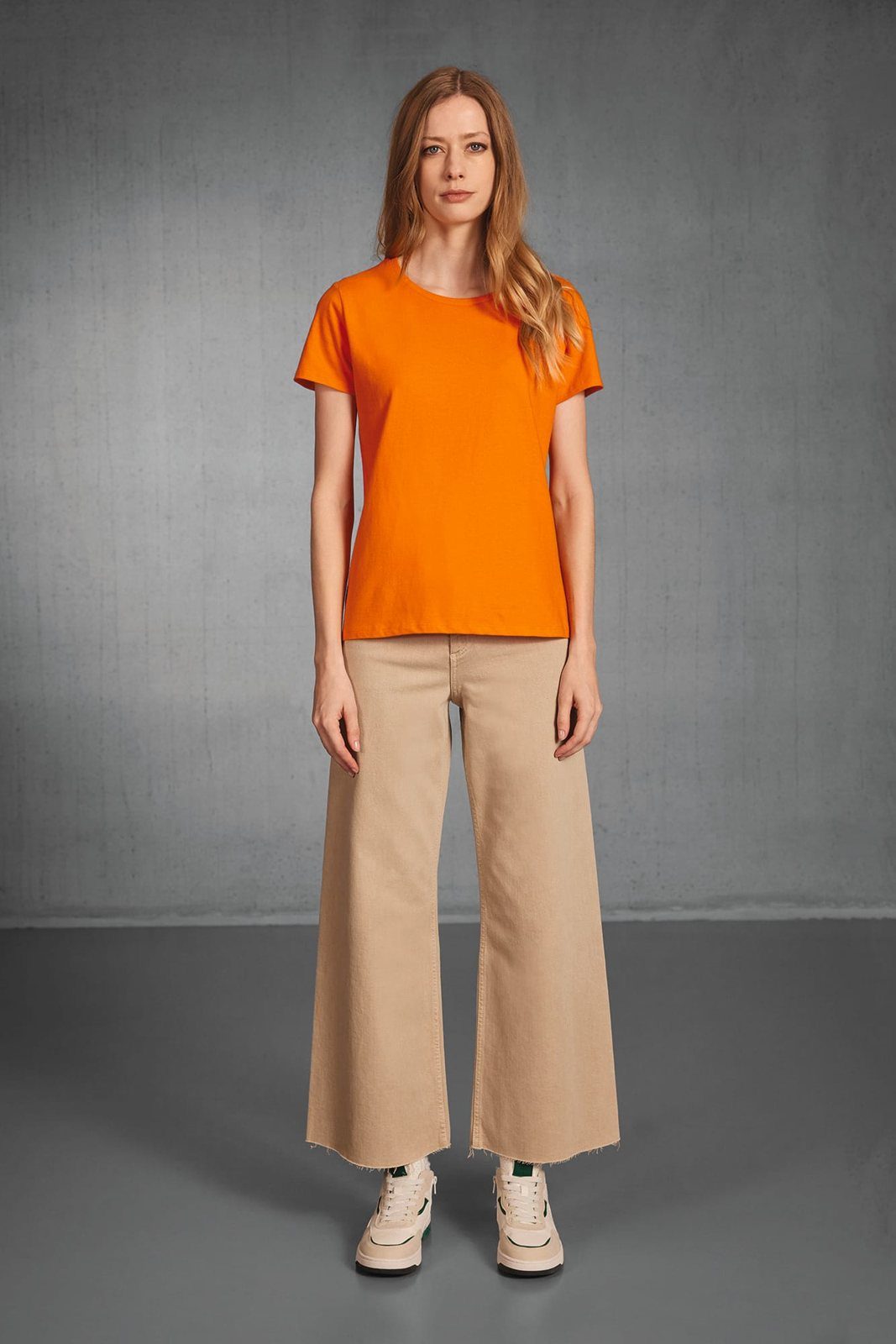 Vrouw in een oranje T-shirt, wijde beige jeans en sneakers