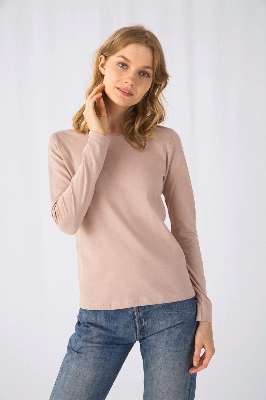 Vrouw met blond haar in een zachtroze shirt met lange mouwen en een jeans