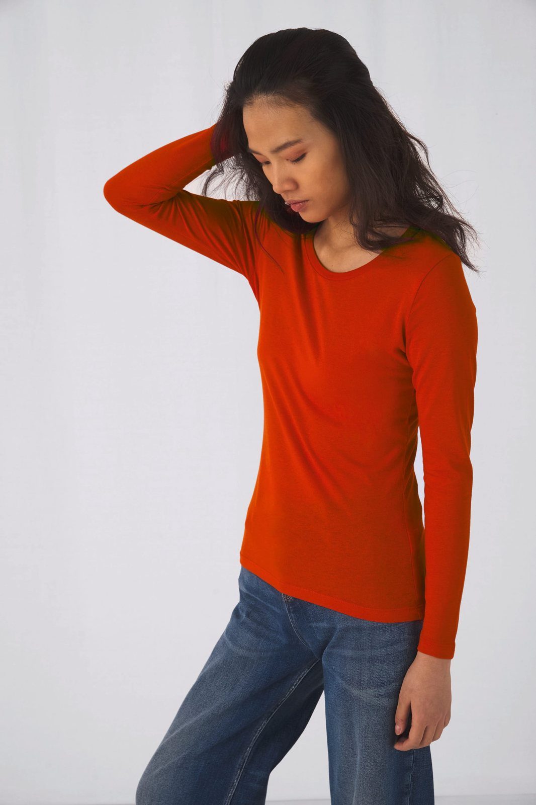 Vrouw met een hand in haar haar in een oranjerood shirt met lange mouwen