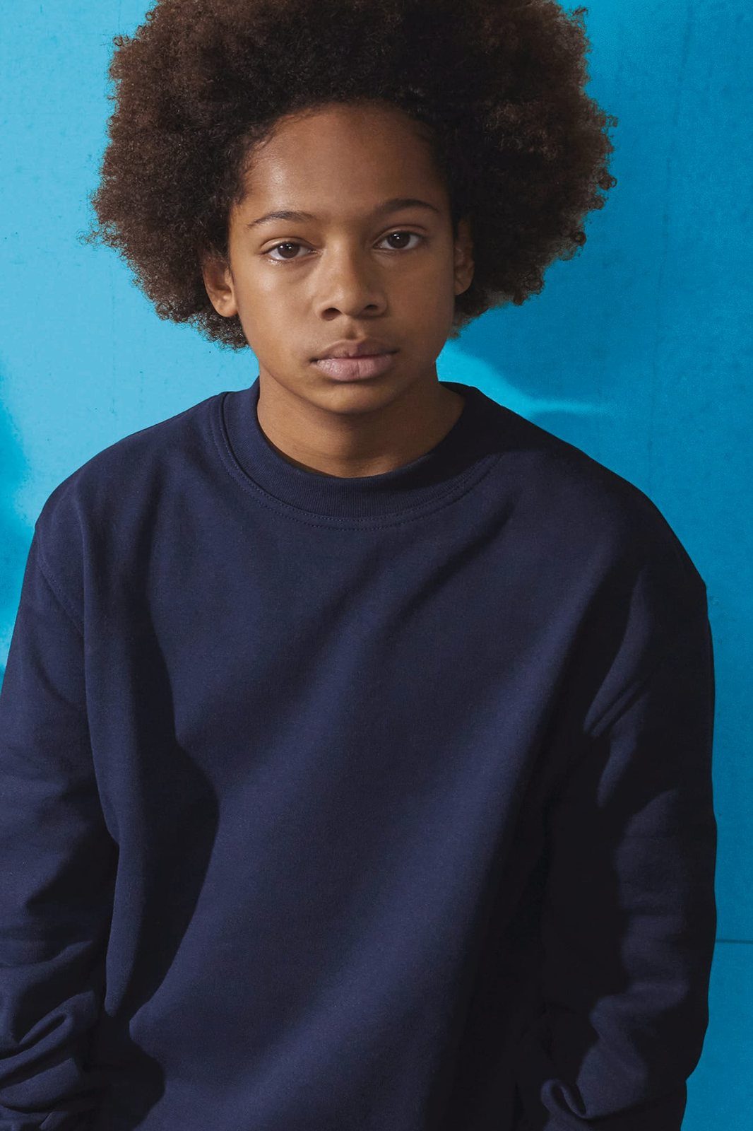 Jongen met afro in een donkerblauwe sweater voor een blauwe muur