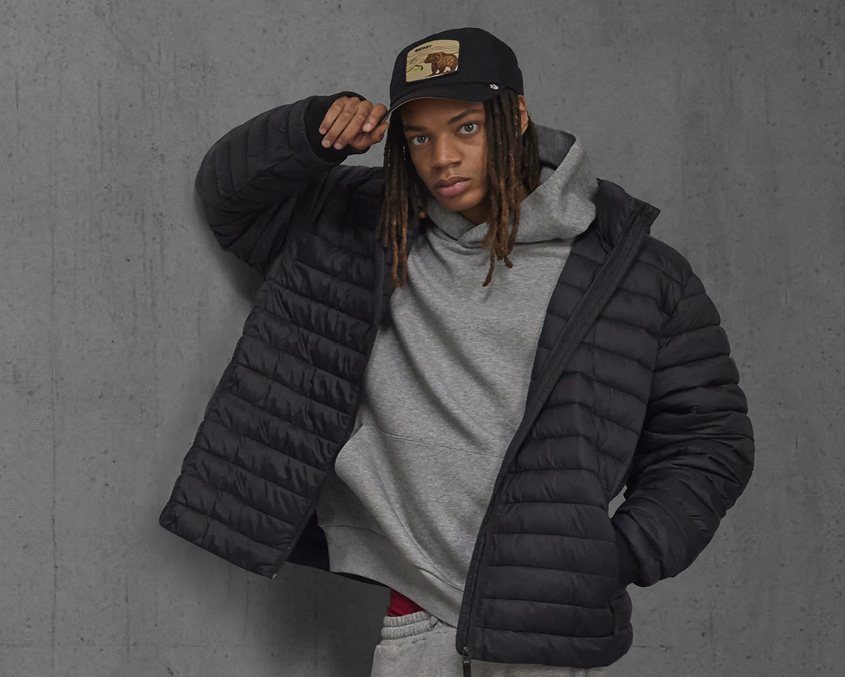 Man met pet in een zwarte gewatteerde jas over een grijze hoodie