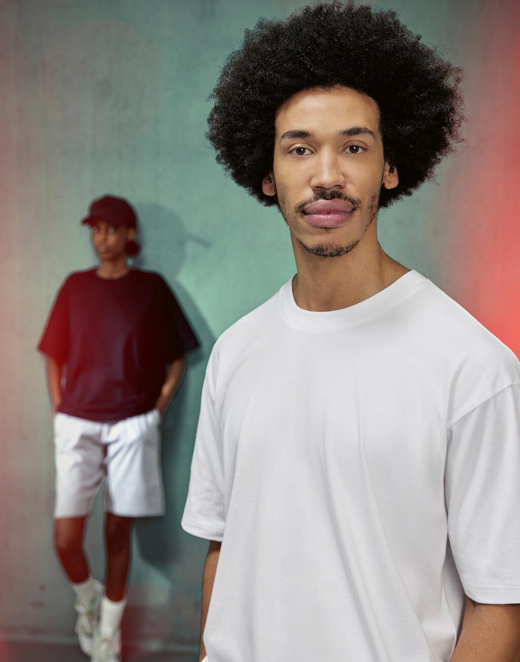 Man in een wit oversized T-shirt, op de achtergrond iemand in bordeaux