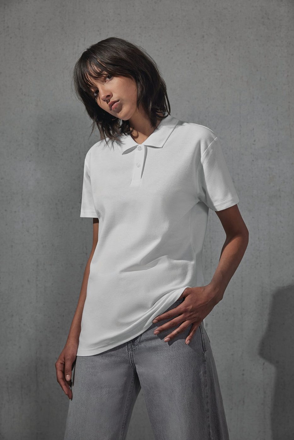 Vrouw in een witte polo tegen een betonnen muur