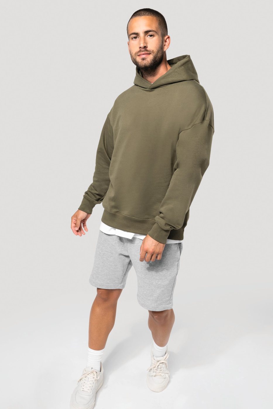 Man in an olive green oversized hoodie with grey shorts