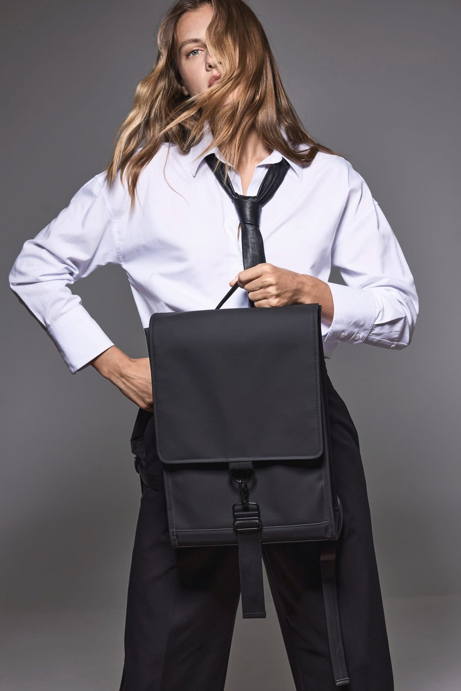 Vrouw in een witte blouse met een zwarte rugzak met klep in haar hand