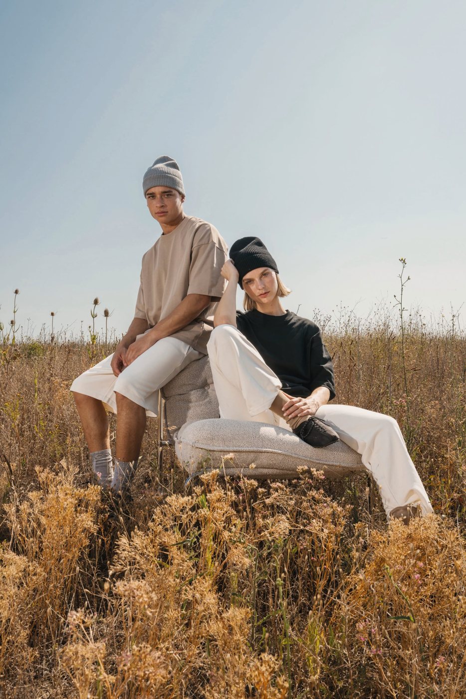 Twee mensen in oversized T-shirts en mutsen zittend in een zomers veld