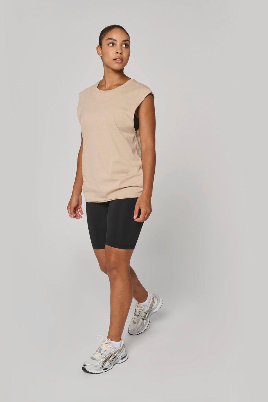 Woman in a sand-coloured sleeveless shirt and black shorts
