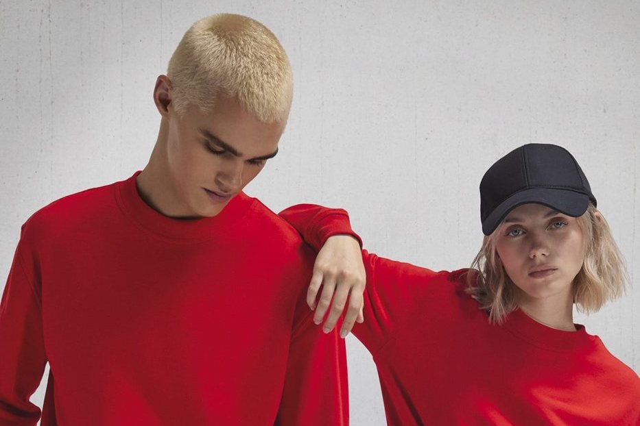 Man en vrouw in dezelfde rode uniseks sweater met ronde hals, zij leunt op zijn schouder