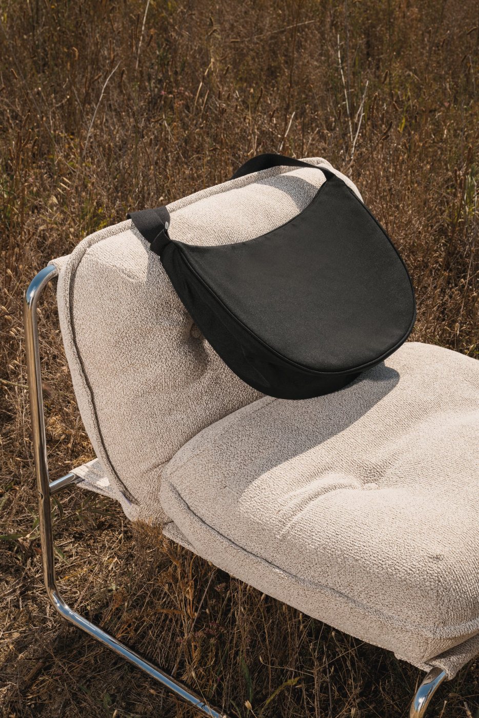 Black half-moon bag on a cream-coloured armchair in a field of dry grass