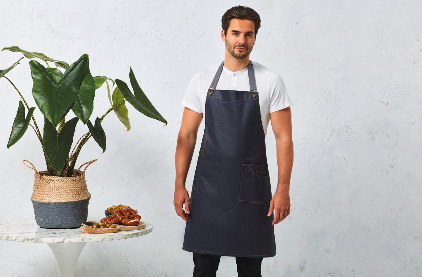 Man in een donkerblauw halterschort in denimlook over een wit T-shirt