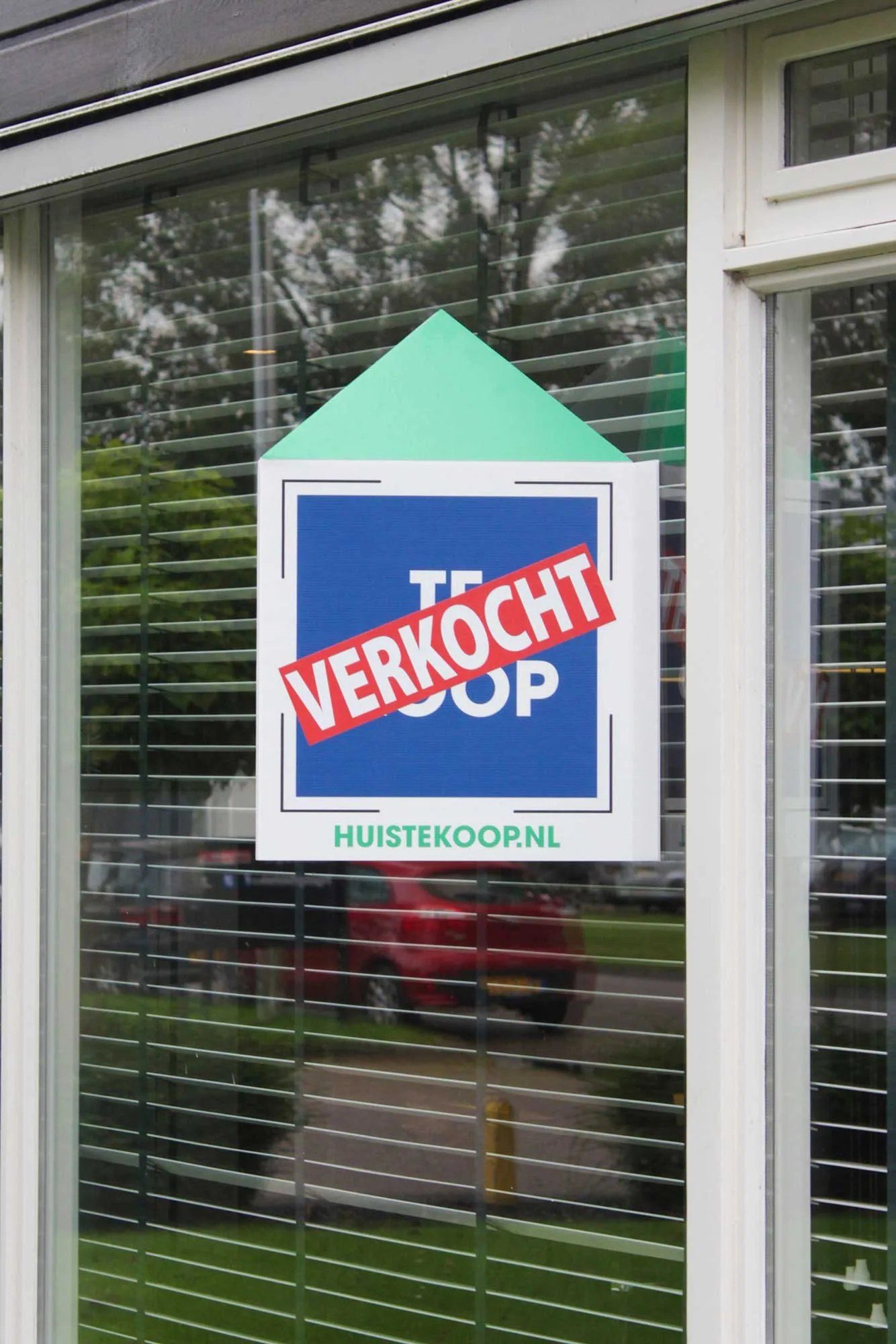 Makelaarsbord met verkocht-sticker achter een raam
