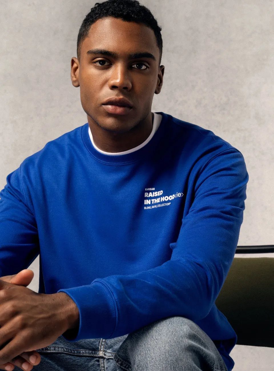 Man in een blauwe Kariban-sweater met een witte print op de borst