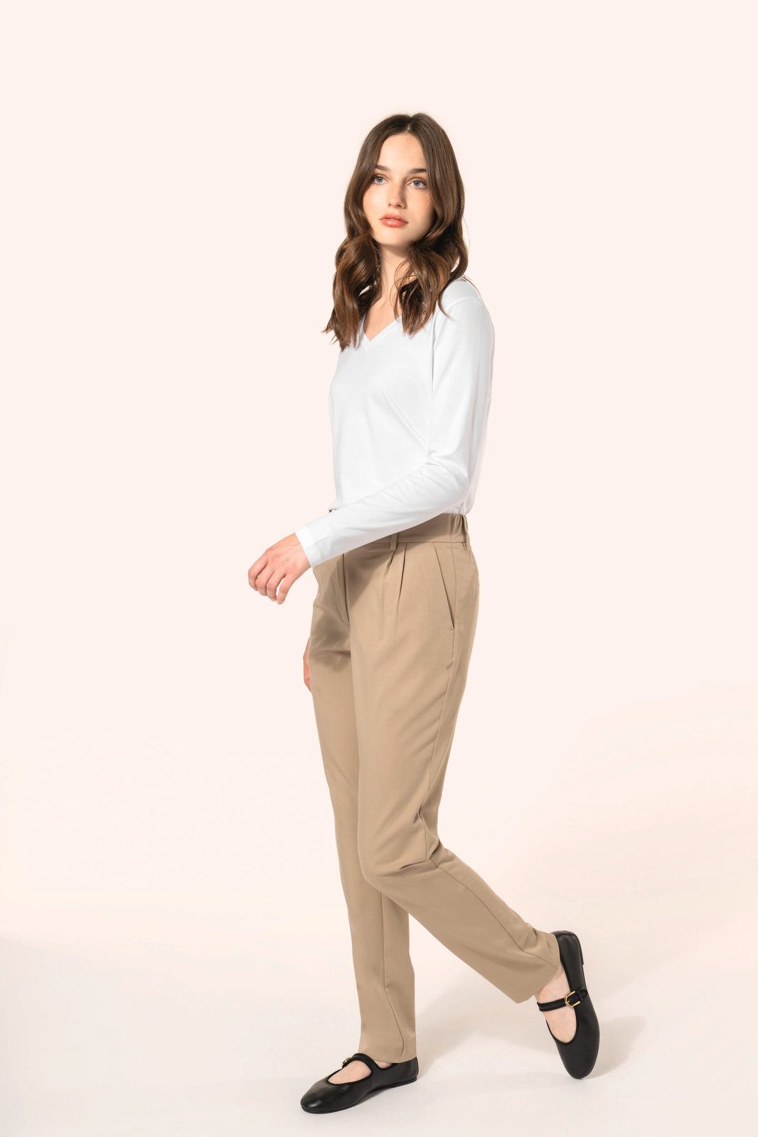 Woman in beige trousers and a white shirt walking through the studio