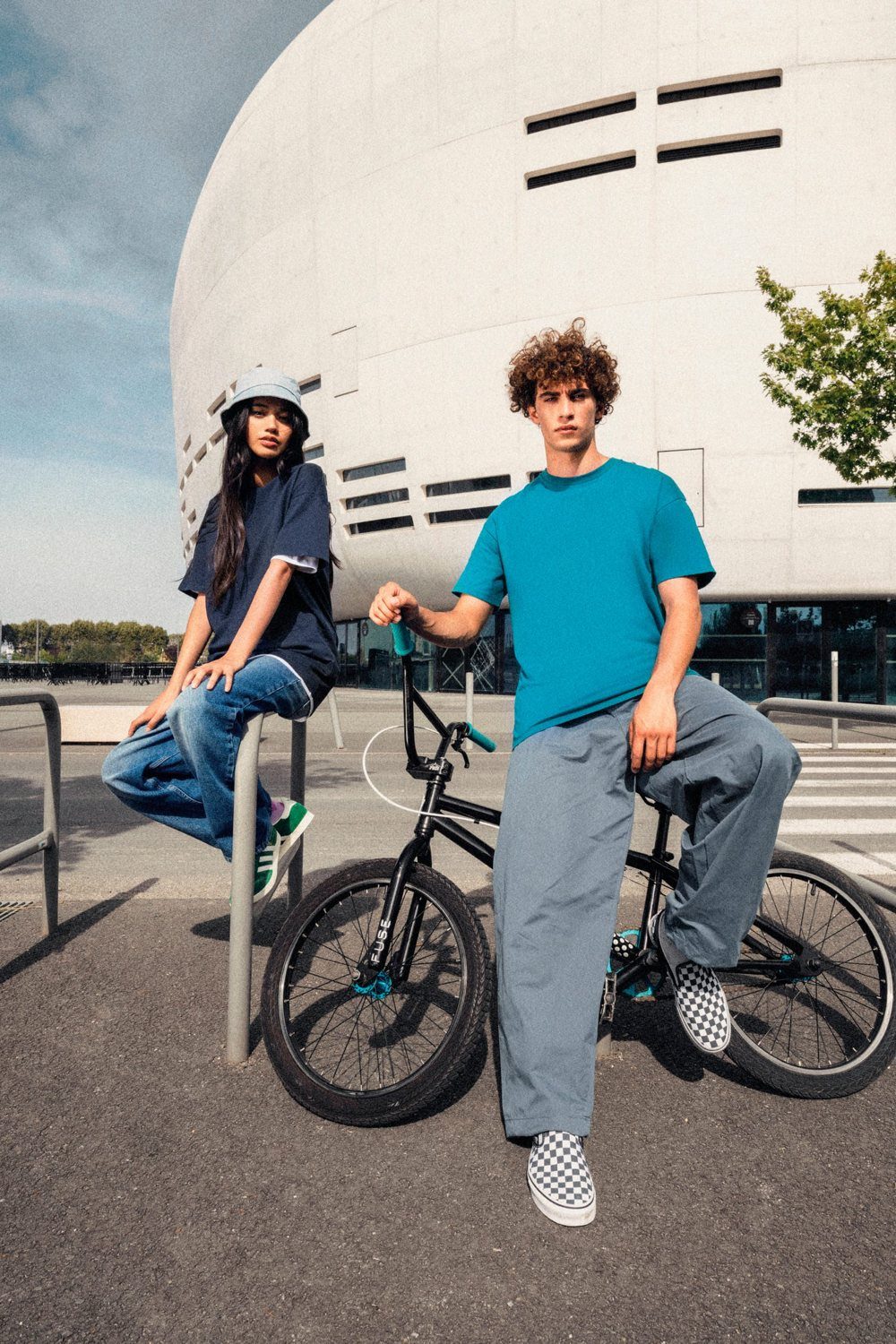 Twee jongeren met een fiets voor een modern gebouw, in Native Spirit-shirts