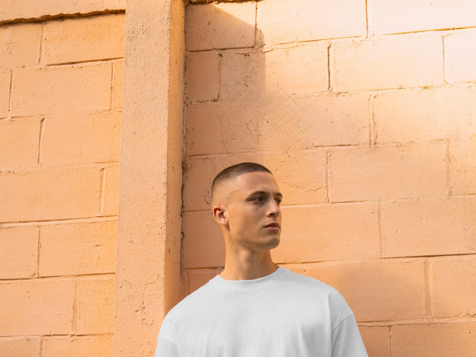 Man in een oversized T-shirt tegen een zonnige muur