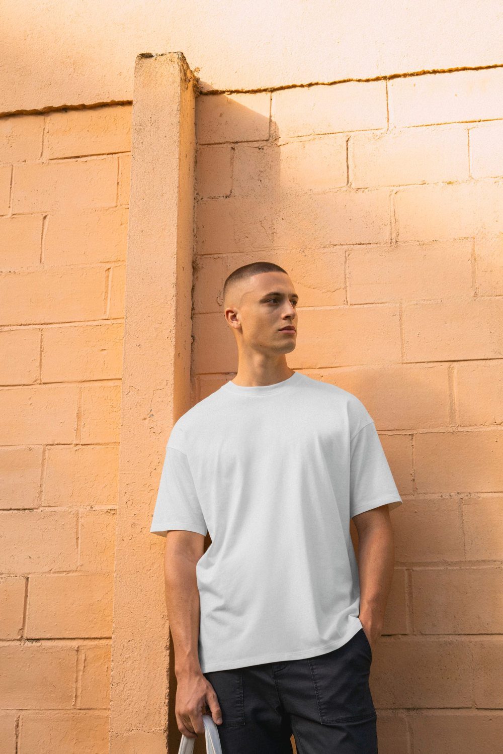 Man in een oversized T-shirt tegen een zonnige muur