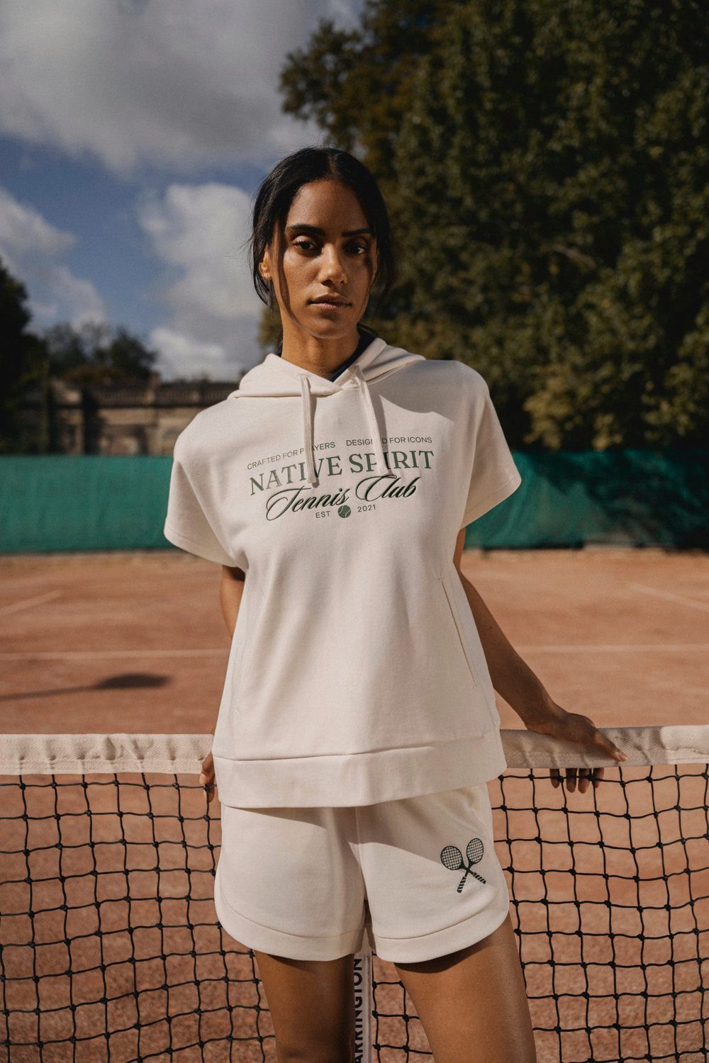 Vrouw in een bedrukte crèmekleurige hoodie op een tennisbaan