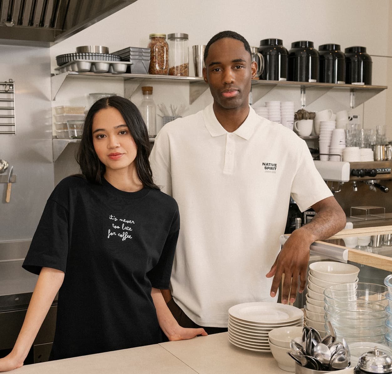 Twee medewerkers in een koffiebar, in een bedrukt zwart T-shirt en een witte polo met logo